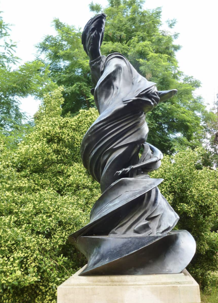 Sculpture en bronze d'un homme formant une spirale ascendante, sur un socle en pierre, avec des arbres en arrière-plan.
