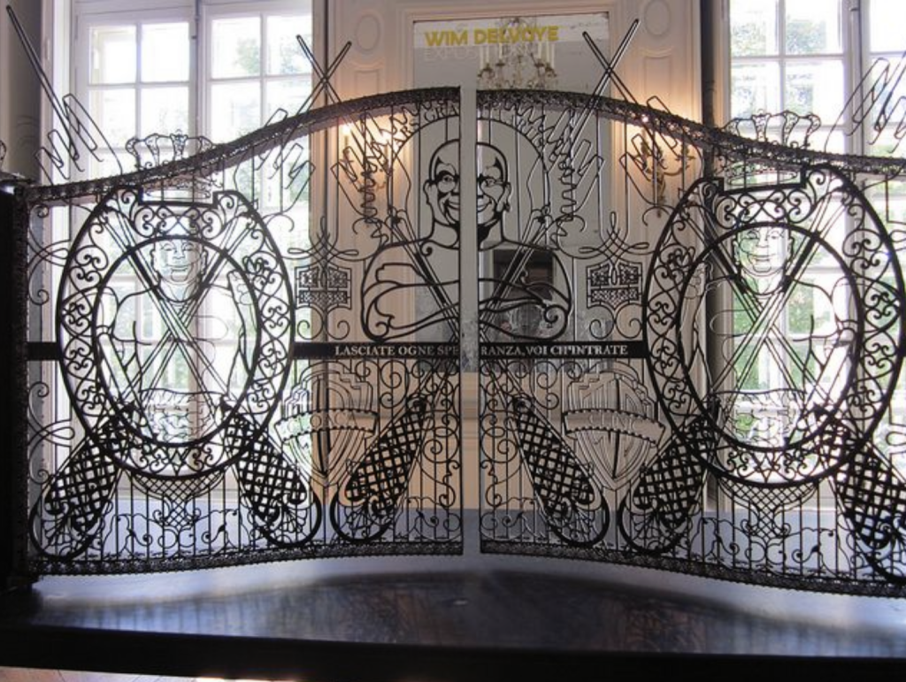 Photo d'un portail en fer forgé à deux vantaux, avec un décor de fourchettes géantes de de bustes de "Monsieur Propre", dans une salle de musée.
